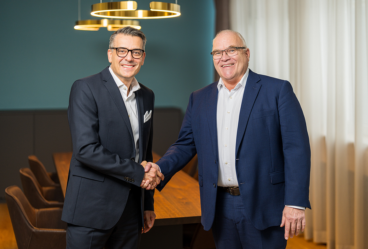 Der neue CEO Oliver Dörre schüttelt Thomas Müller die Hand. Beide schauen lächelnd in die Kamera